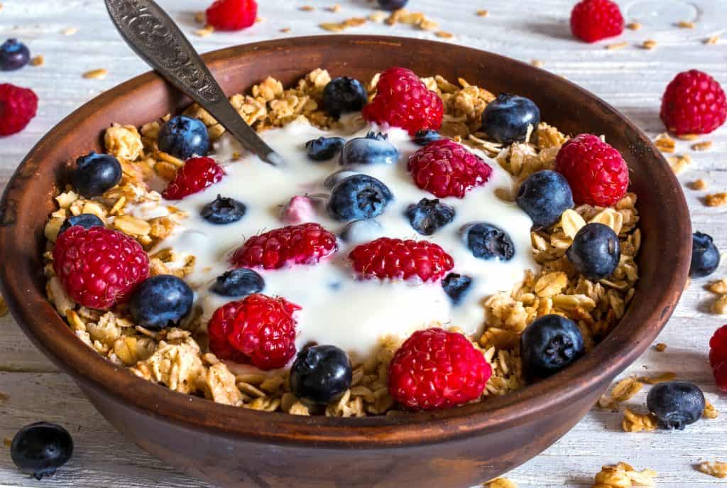 bowl of oat granola with yogurt, fresh raspberries, blueberries and nuts with spoon